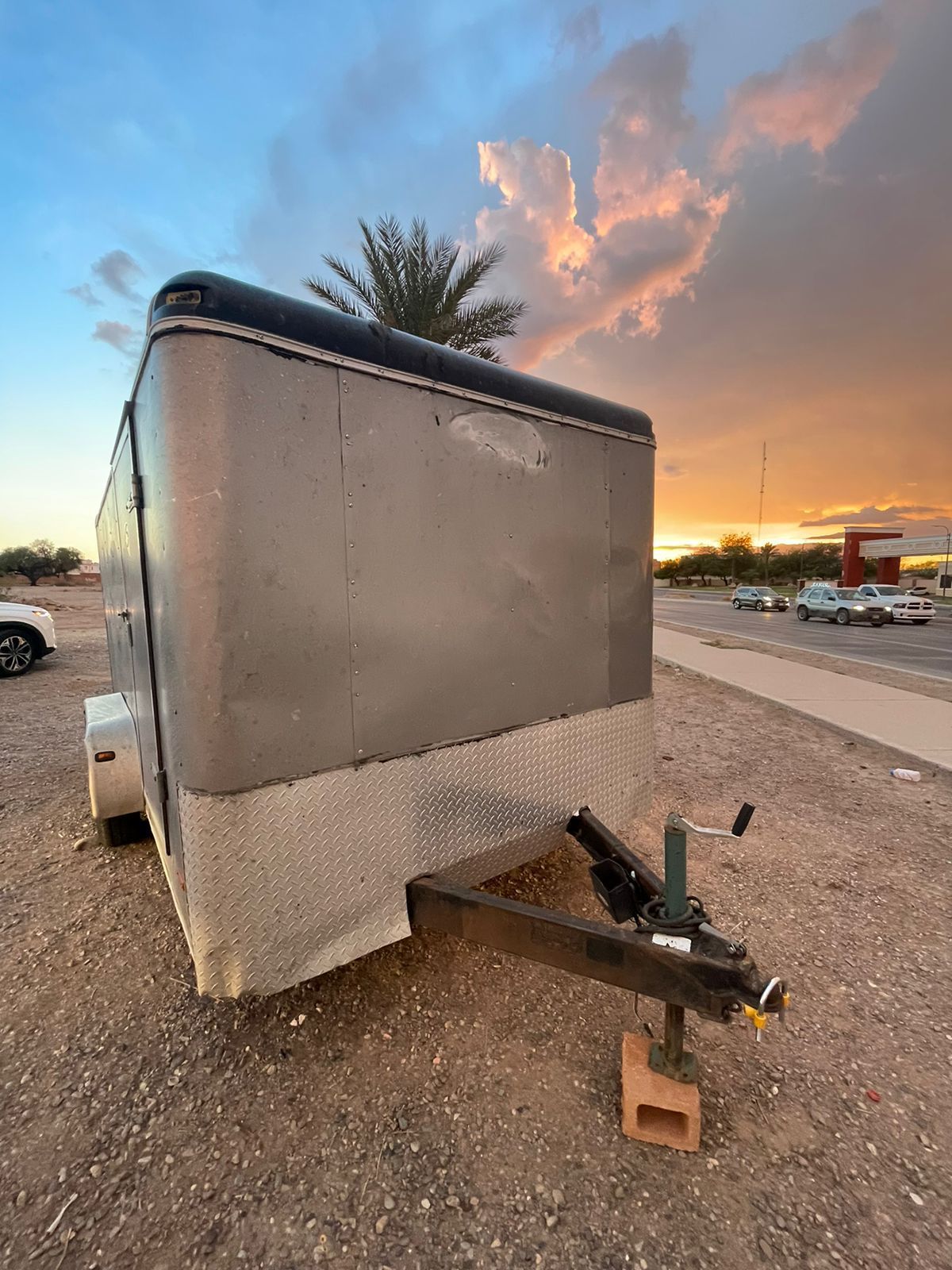 Un remolque está estacionado en un lote de tierra con una palmera al fondo.