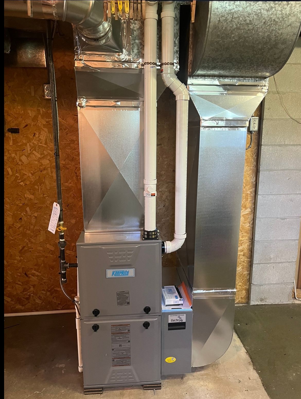 A furnace is sitting in a basement next to a wall.