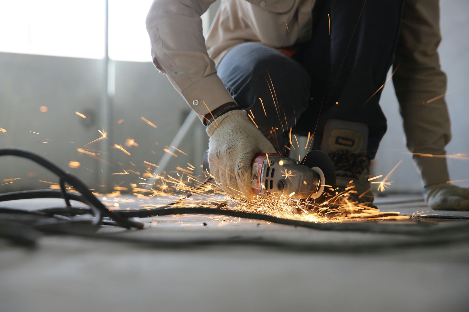 A man is using a grinder to cut a piece of metal on the floor.