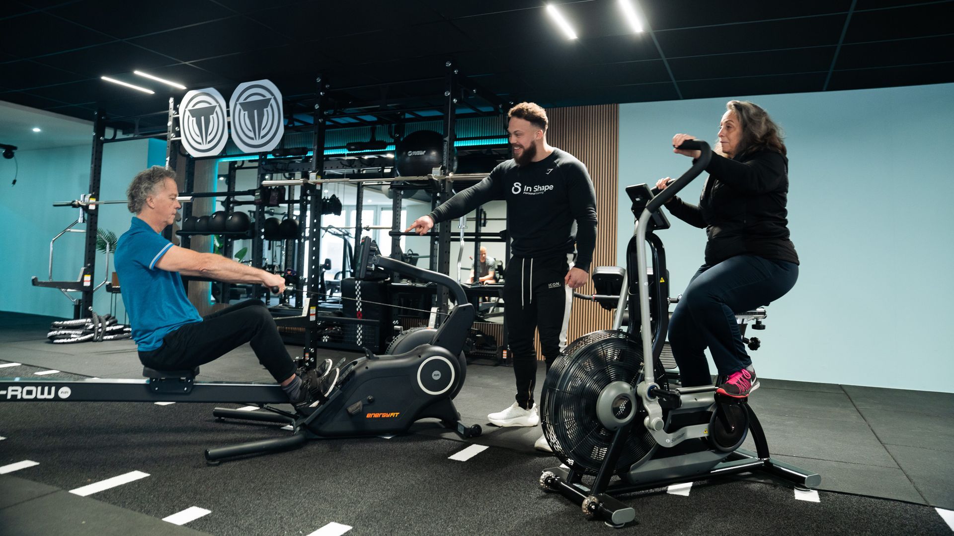 A man demonstrating exercise equipment to two people at a gym.