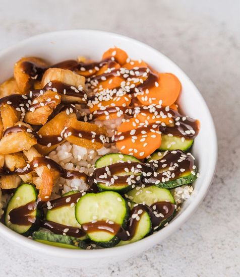 A bowl of rice with chicken and carrots and cucumbers and sesame seeds