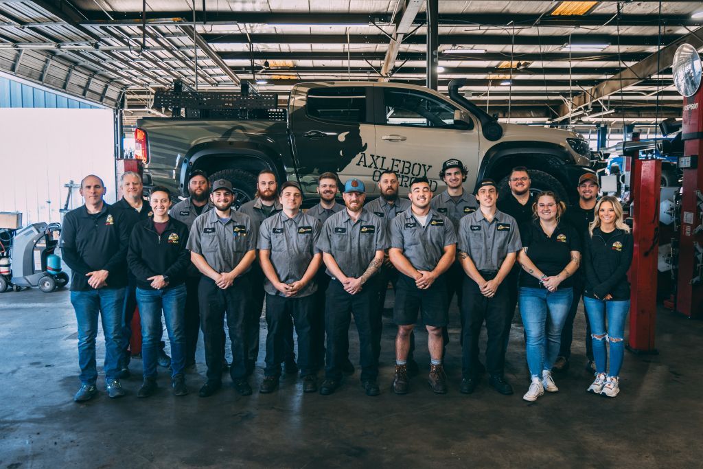 Group of mechanics in a garage, standing in front of a customized truck. Some are smiling, wearing uniforms.