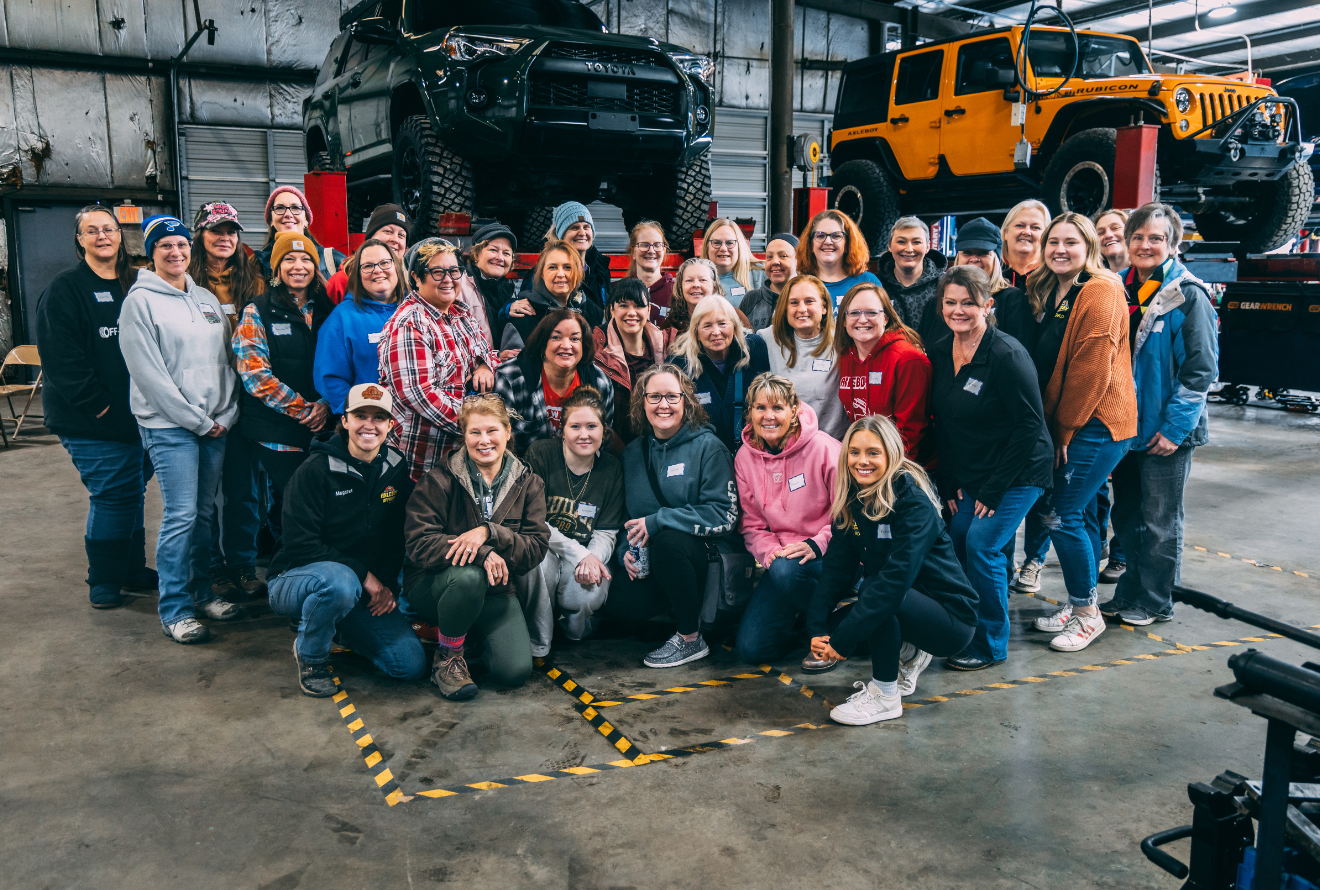 Group of people, wearing grey shirts, posing in an industrial setting, smiling, one person lying down.