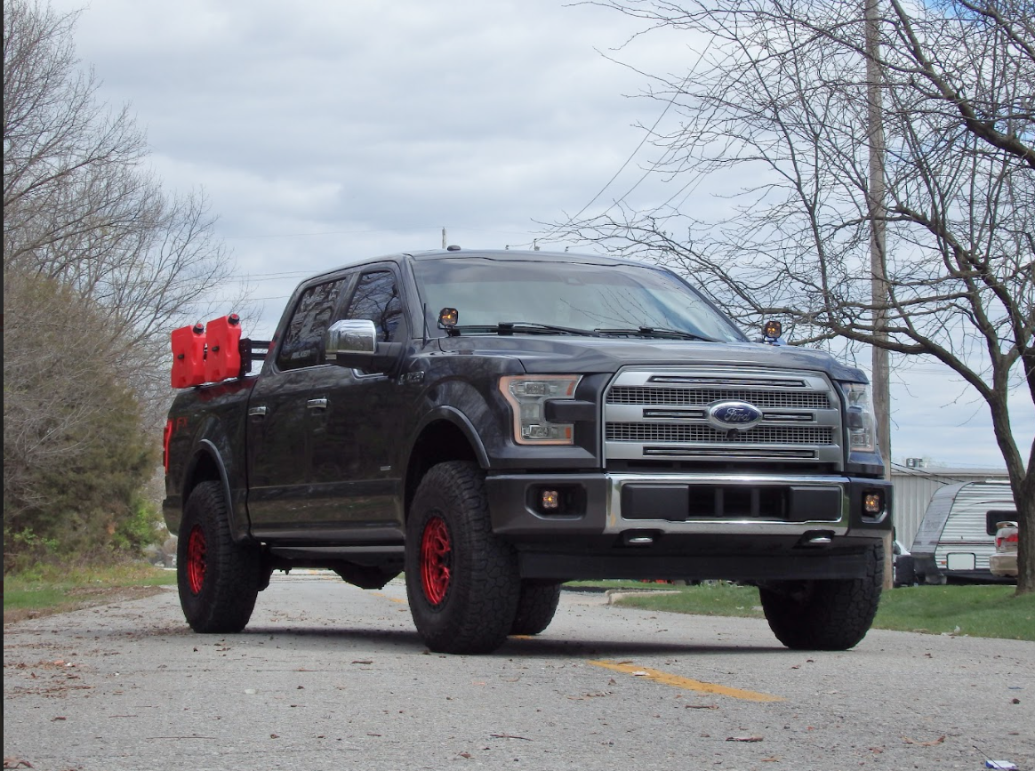 Man working at a cluttered desk with multiple computer screens.  He is looking at the screens, in an indoor setting.