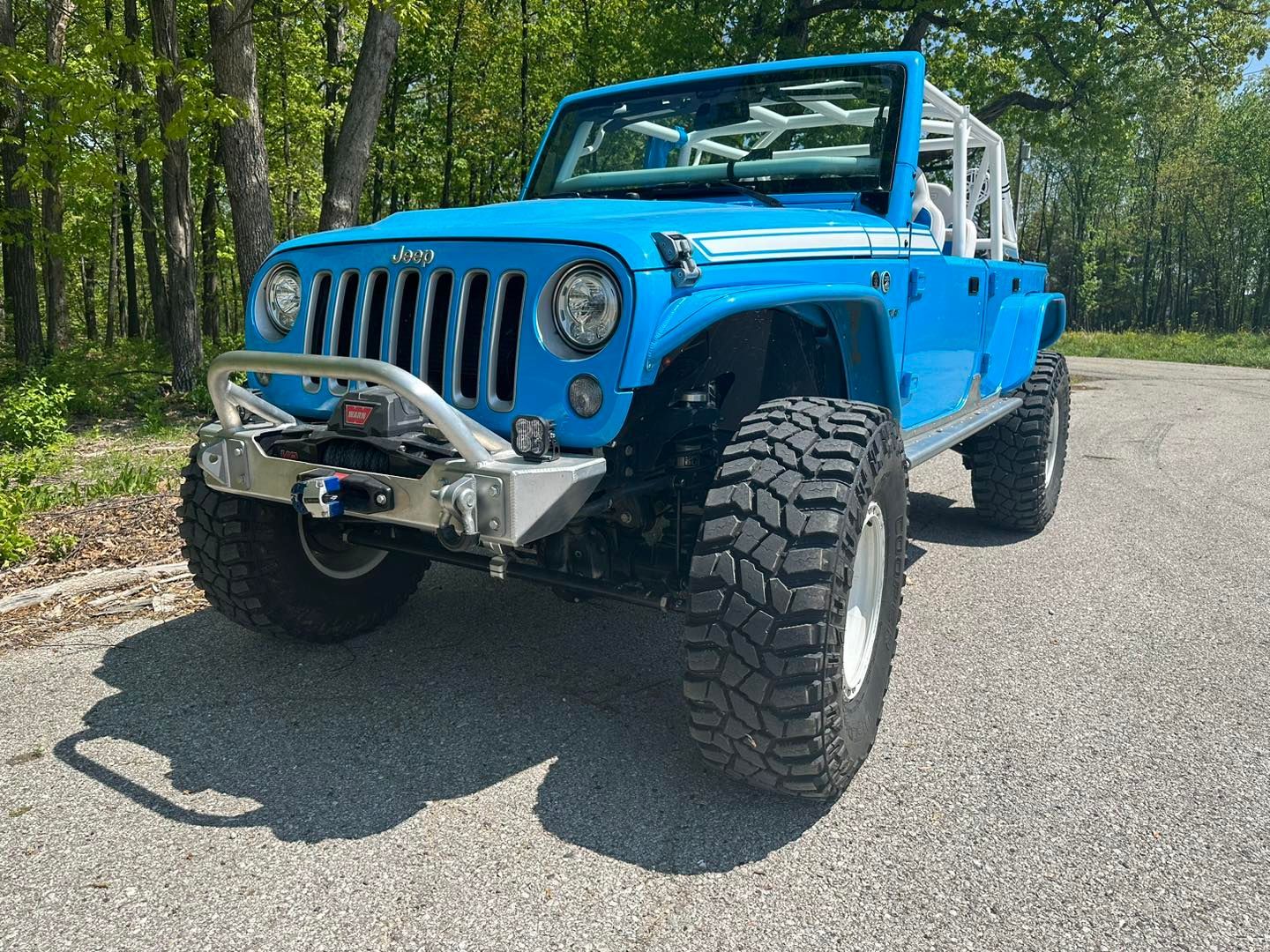 Bright blue Jeep Wrangler, heavily modified with large tires and roll cage, parked on pavement.