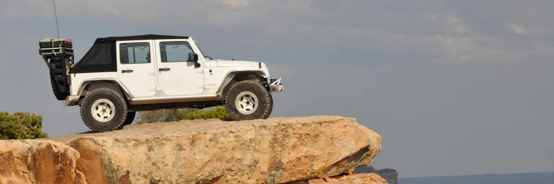 White Jeep Wrangler on a cliff edge, off-roading in a desert landscape.