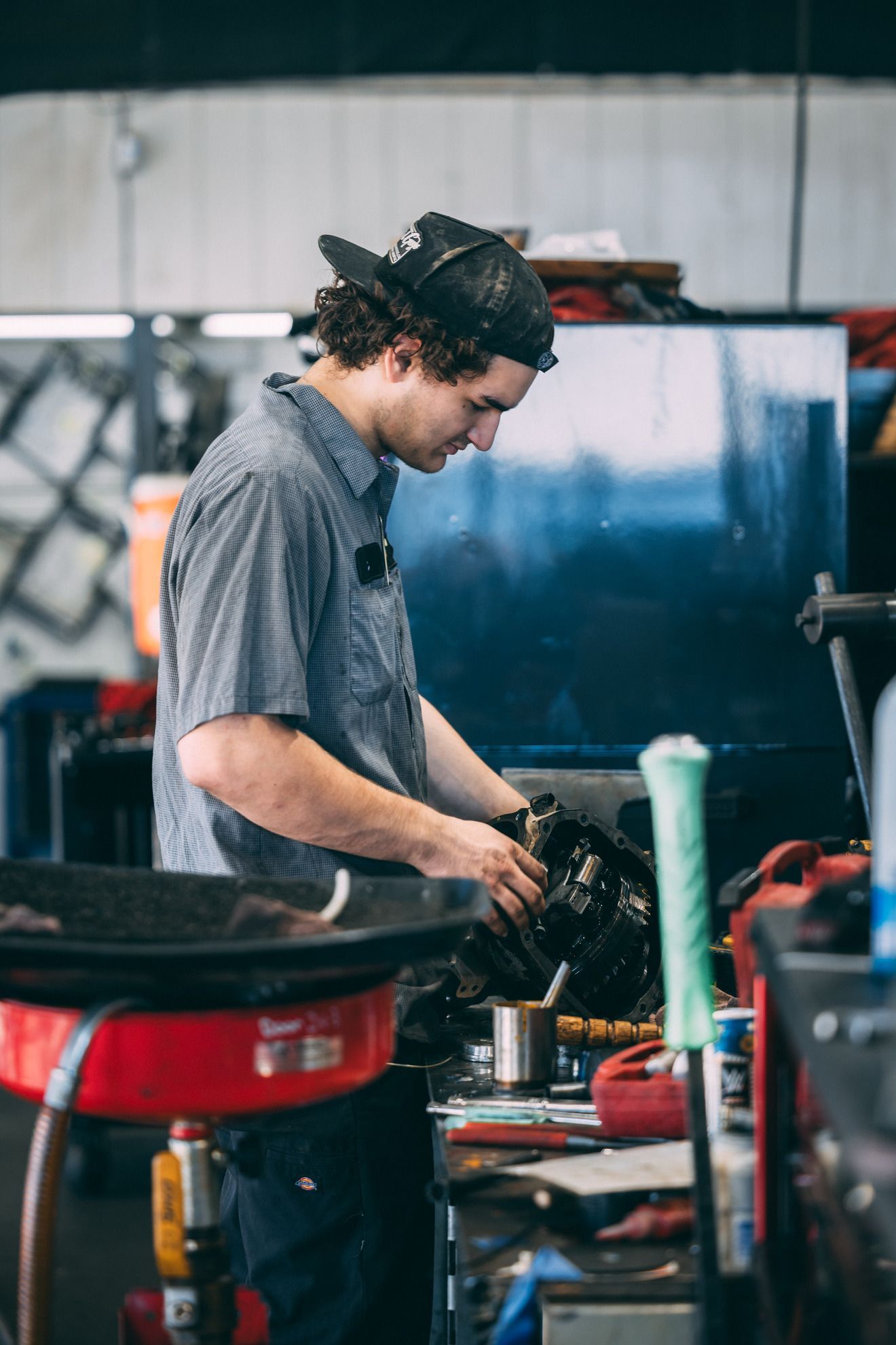 Mechanic in a garage wearing a hat, working on a vehicle, inspecting parts.