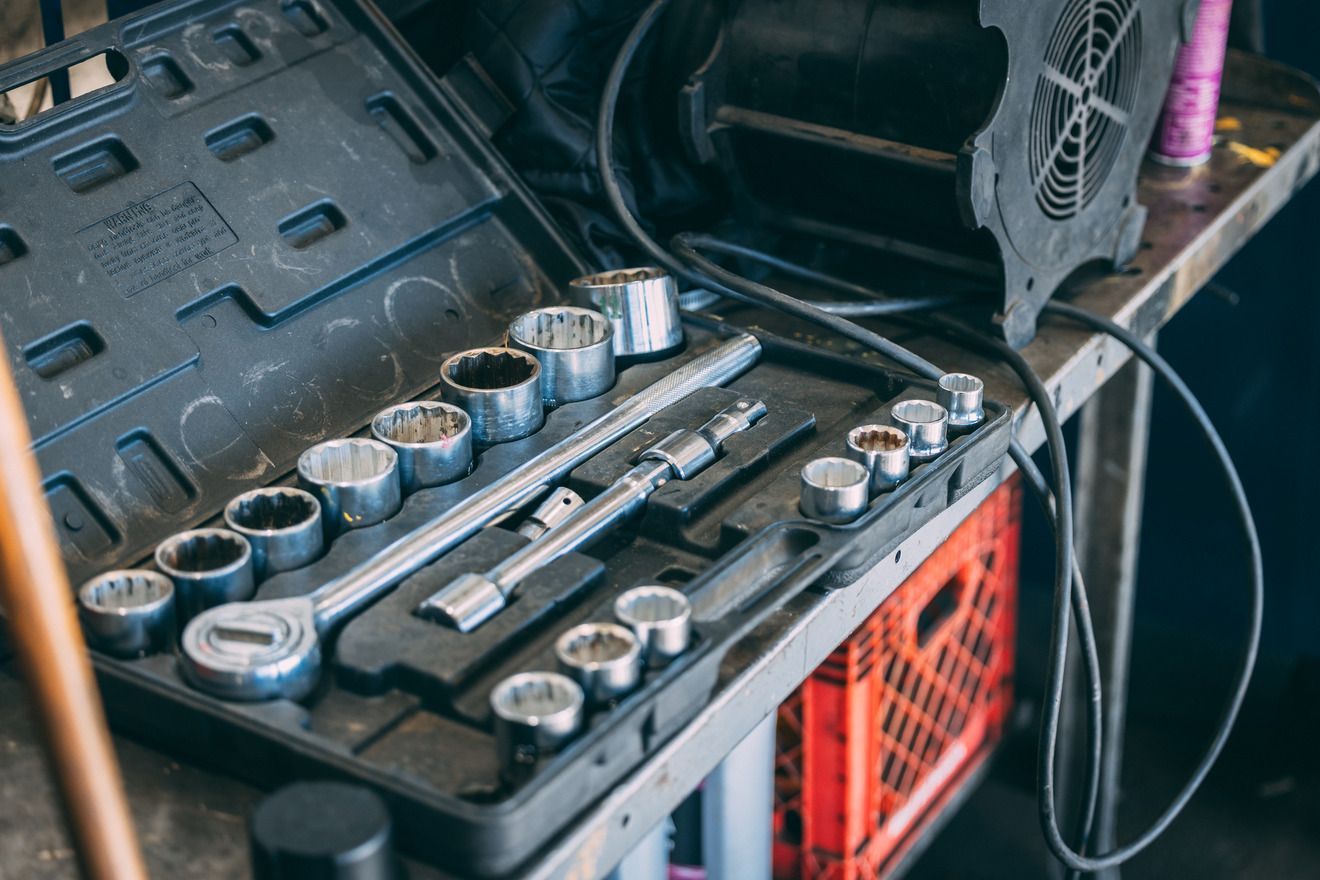 Open toolbox with sockets and ratchet wrench on a workbench, next to a fan and crate.