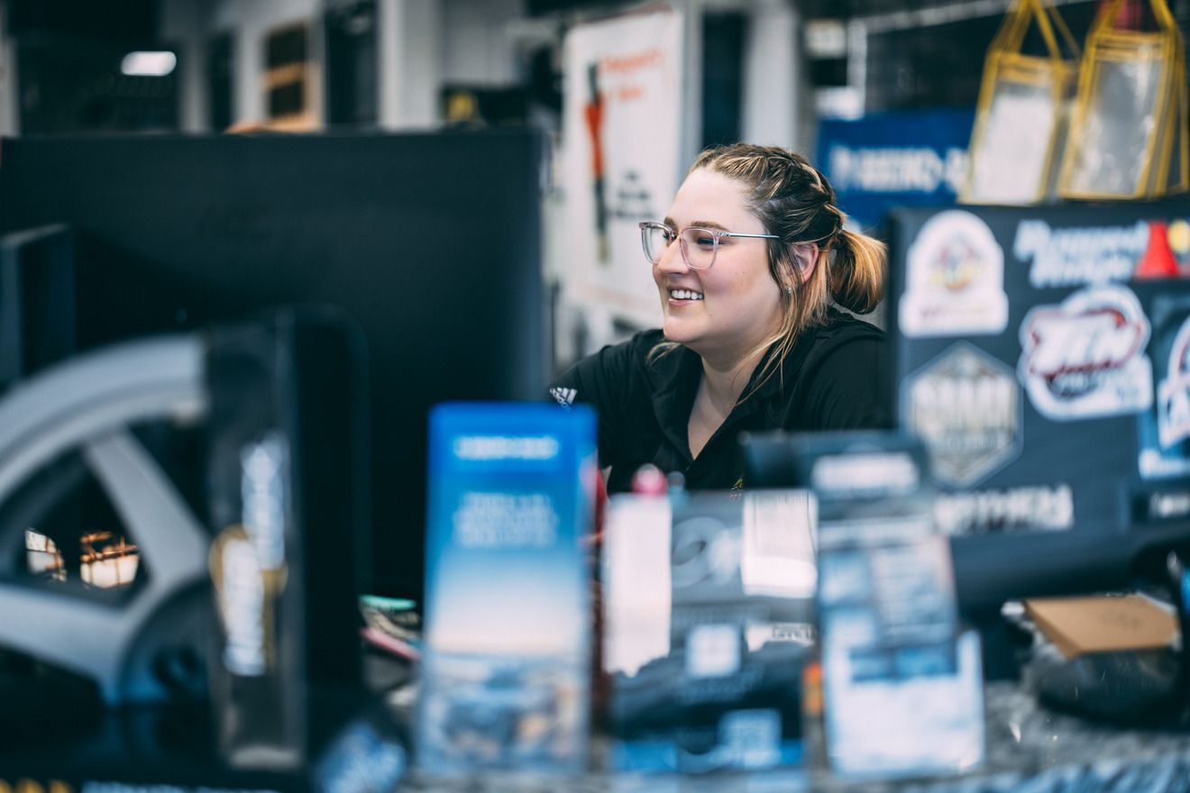 Woman wearing glasses smiles while working at a desk with various items.