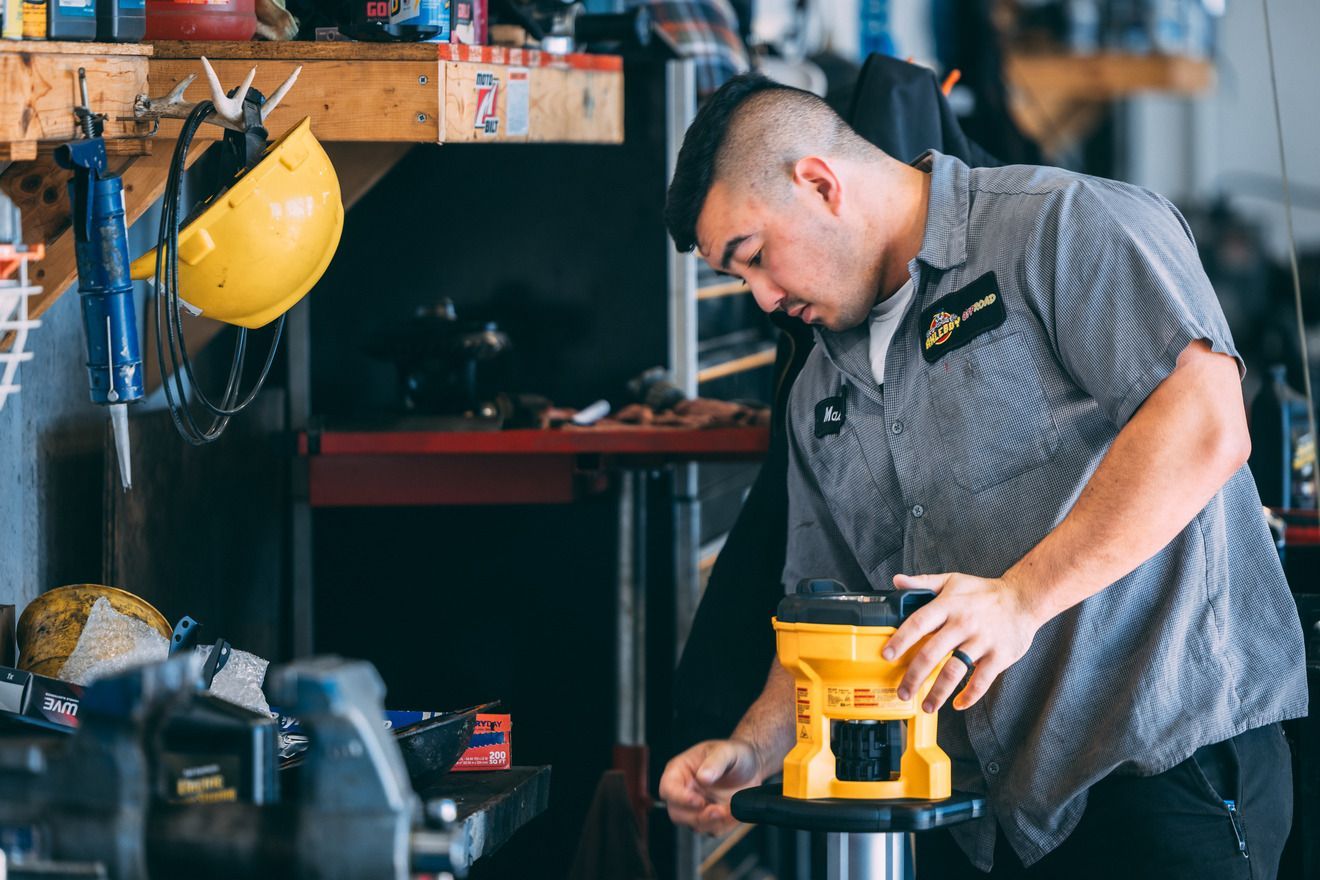Mechanic working on equipment in a garage, focused and attentive, wearing a grey shirt.