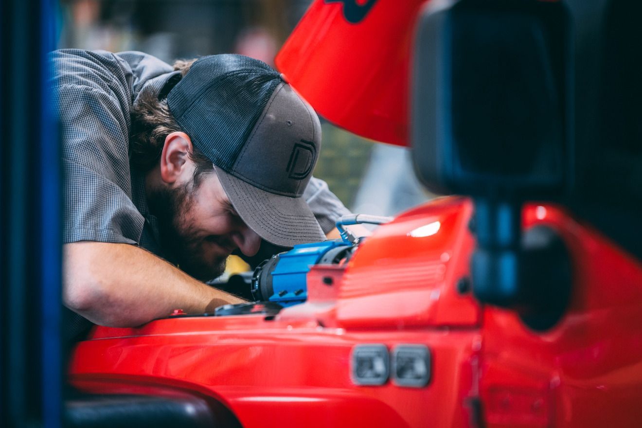 Man in cap leans over a red car engine, working with tools.