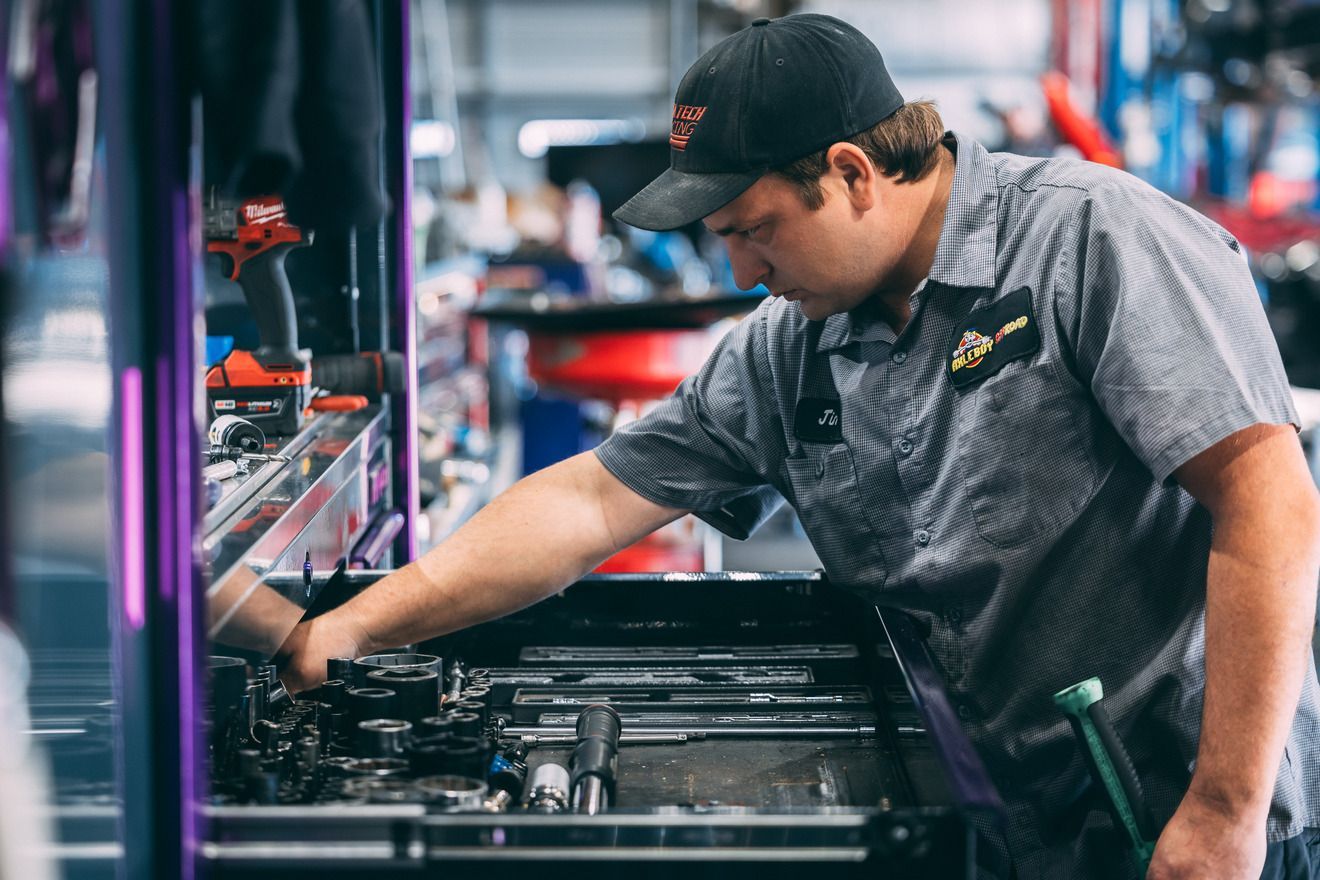 Mechanic in a gray uniform and cap working on machinery in a garage.