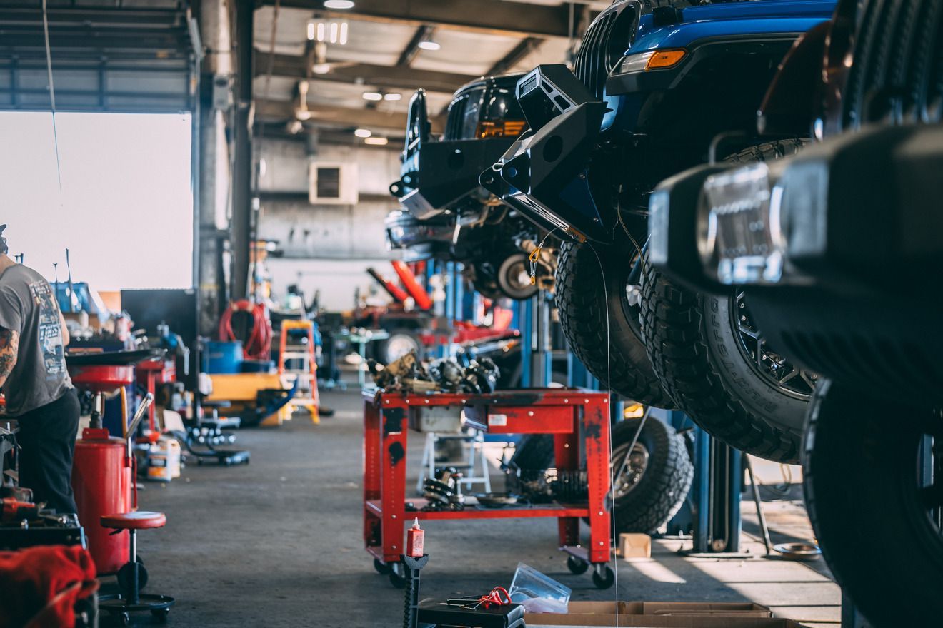 Cars on lifts in a busy auto repair shop with tools and a worker.