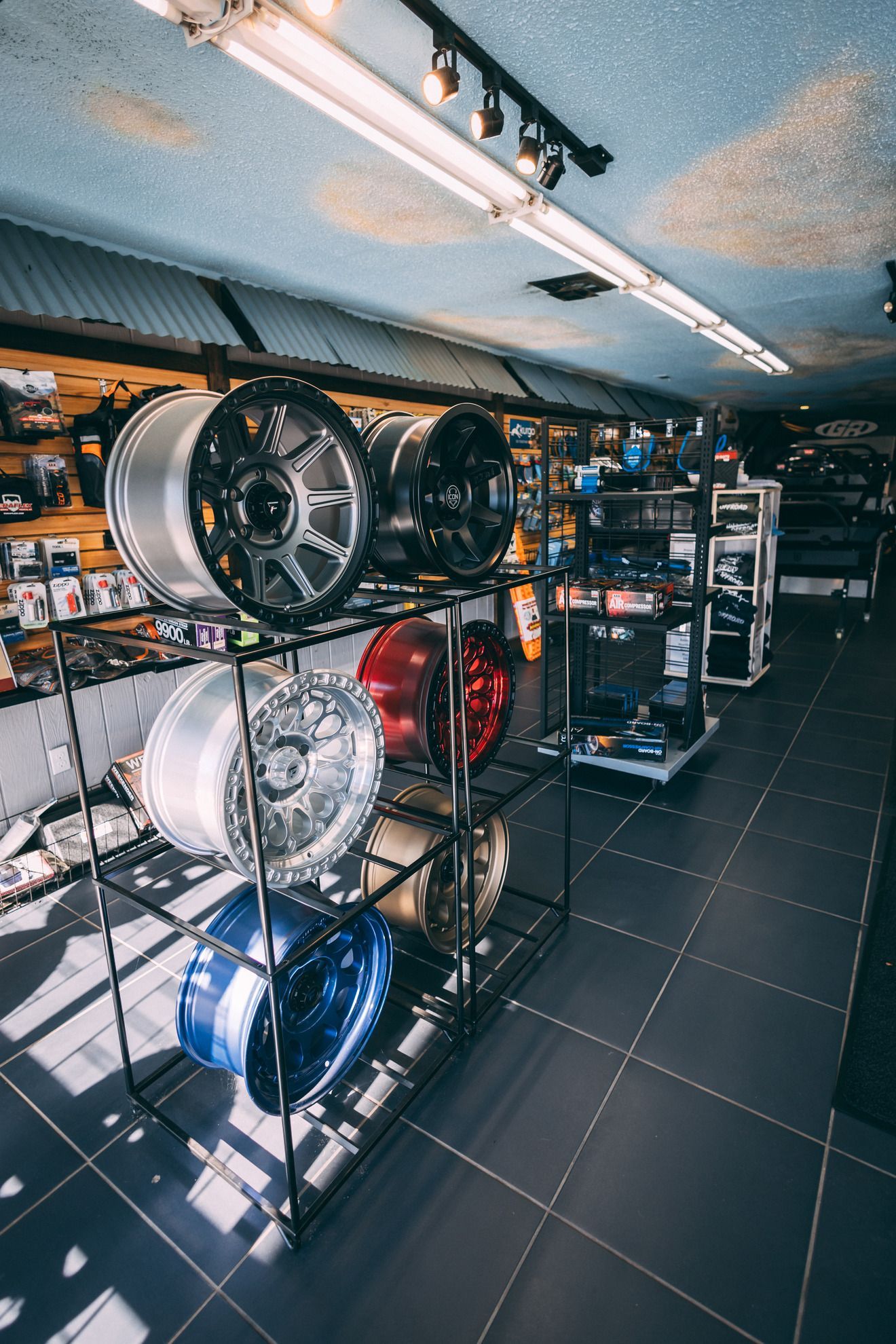 Car rims on display in a shop; various colors and styles, arranged on shelves, and a ceiling with lights.