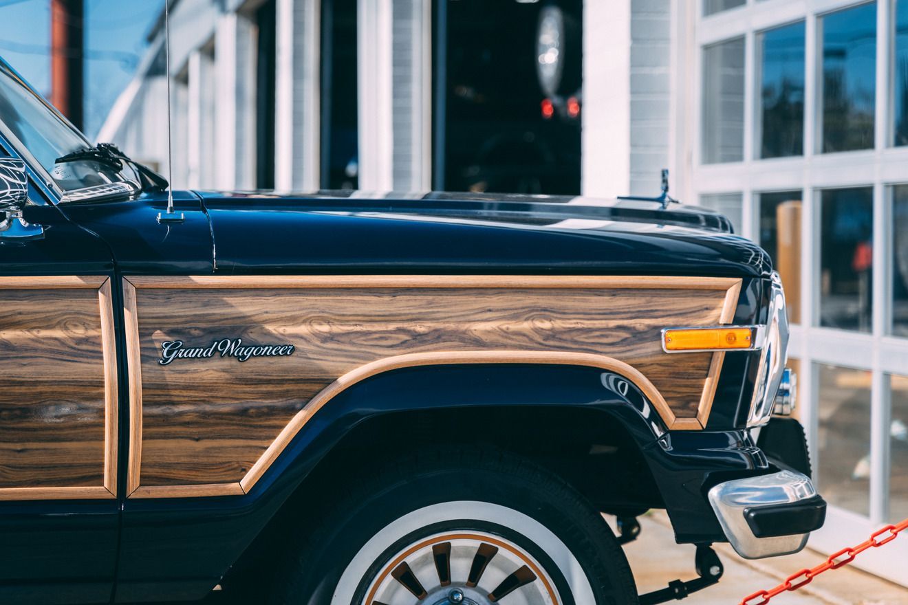 Dark blue Jeep Grand Wagoneer with wood paneling parked near a building.