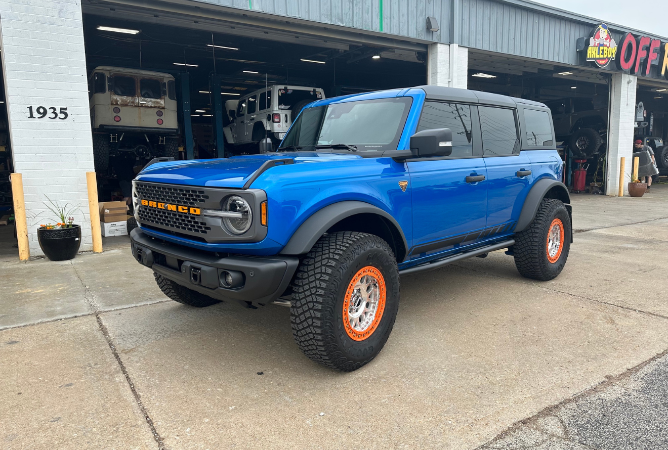 Blue Ford Bronco with orange accented wheels parked outside a repair shop.