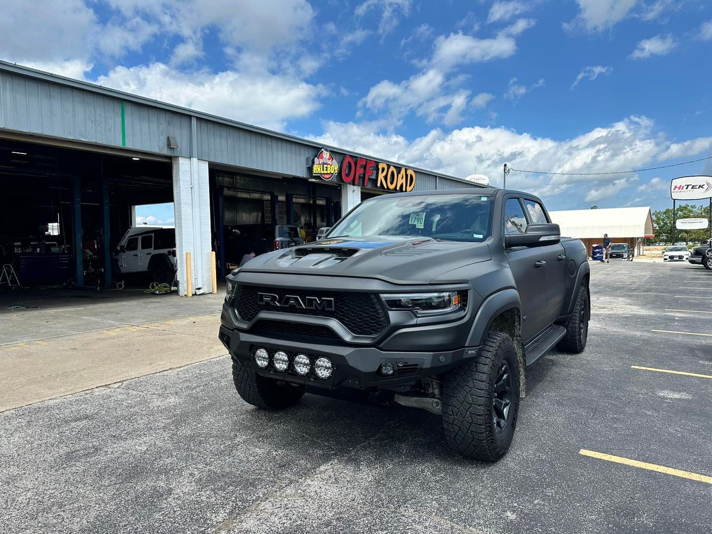 A customized dark gray pickup truck with lifted suspension, four LED auxiliary lights integrated