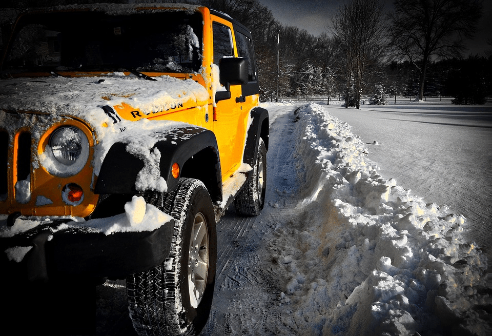 Yellow Jeep Wrangler in snow, driving beside a snowbank.