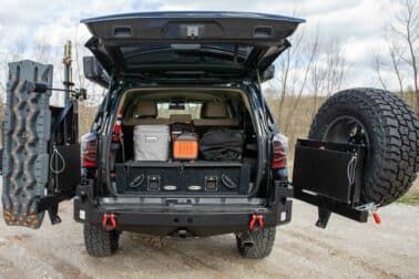 Black SUV with rear hatch open, showing off-road gear: spare tire, traction boards, and storage.