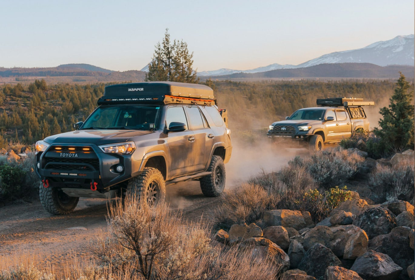 Overlanding - Gray Toyota 4Runner driving on a dirt road, with rooftop tent and two other vehicles in the background.
