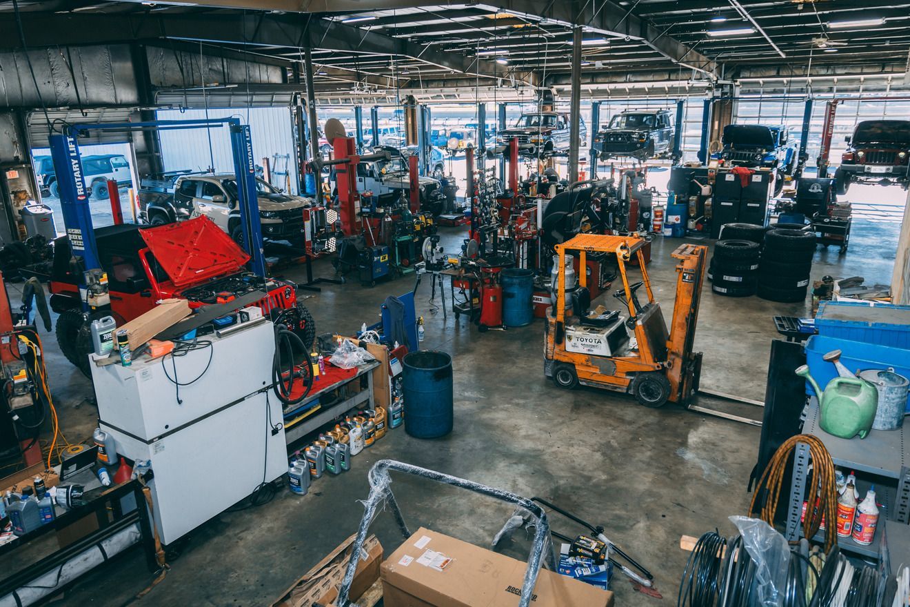 Busy auto repair shop interior with cars on lifts, machinery, and a forklift.