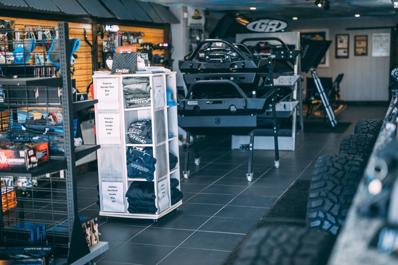 Inside a store, a display of shirts, a black vehicle frame, and tires on the floor.