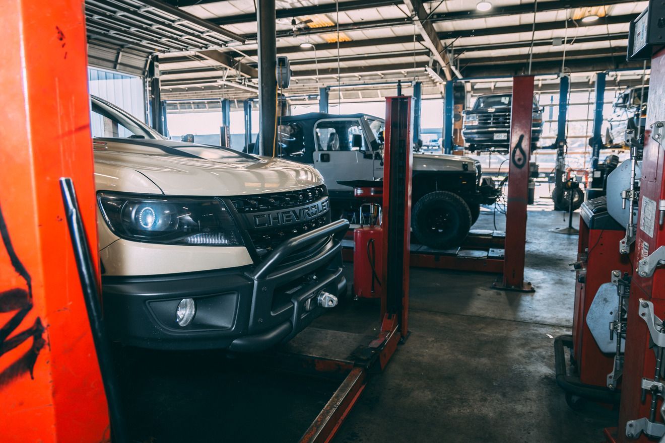 Inside a car repair shop: a tan truck and white Jeep on lifts.