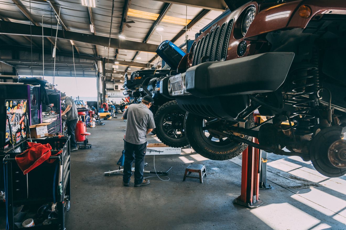 Mechanic working on a lifted Jeep inside a brightly lit auto repair shop.