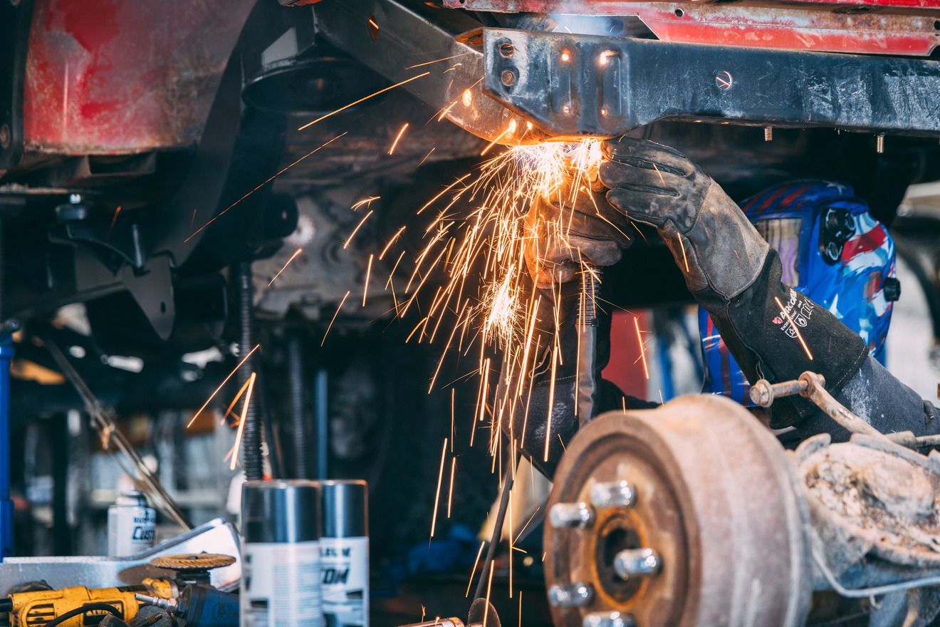 Person welding a car, producing sparks. They wear protective gear in a repair shop.