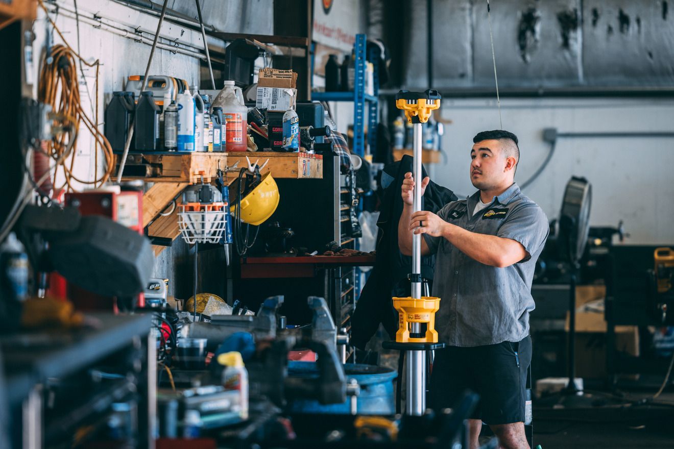 Mechanic in auto shop holding a yellow and black support pole, surrounded by tools and equipment.