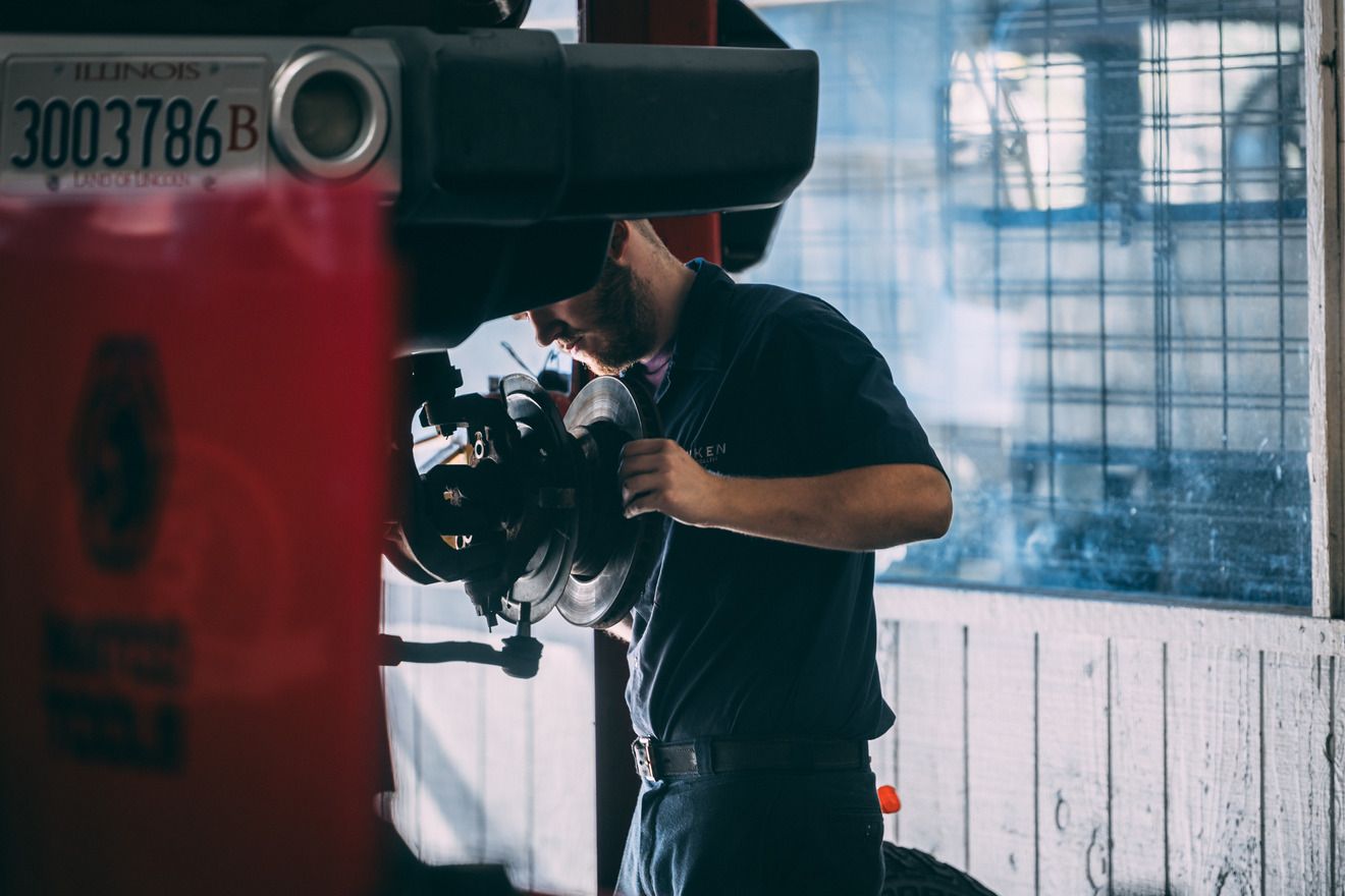 Mechanic working on a car's brakes in a garage. A red lift, California license plate visible.