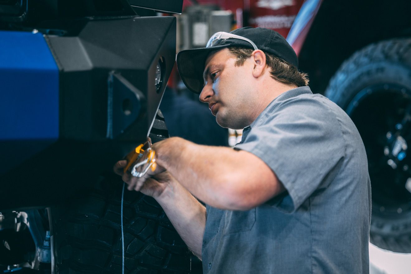 Mechanic in a garage working on a black and blue vehicle, wearing a cap and using tools.