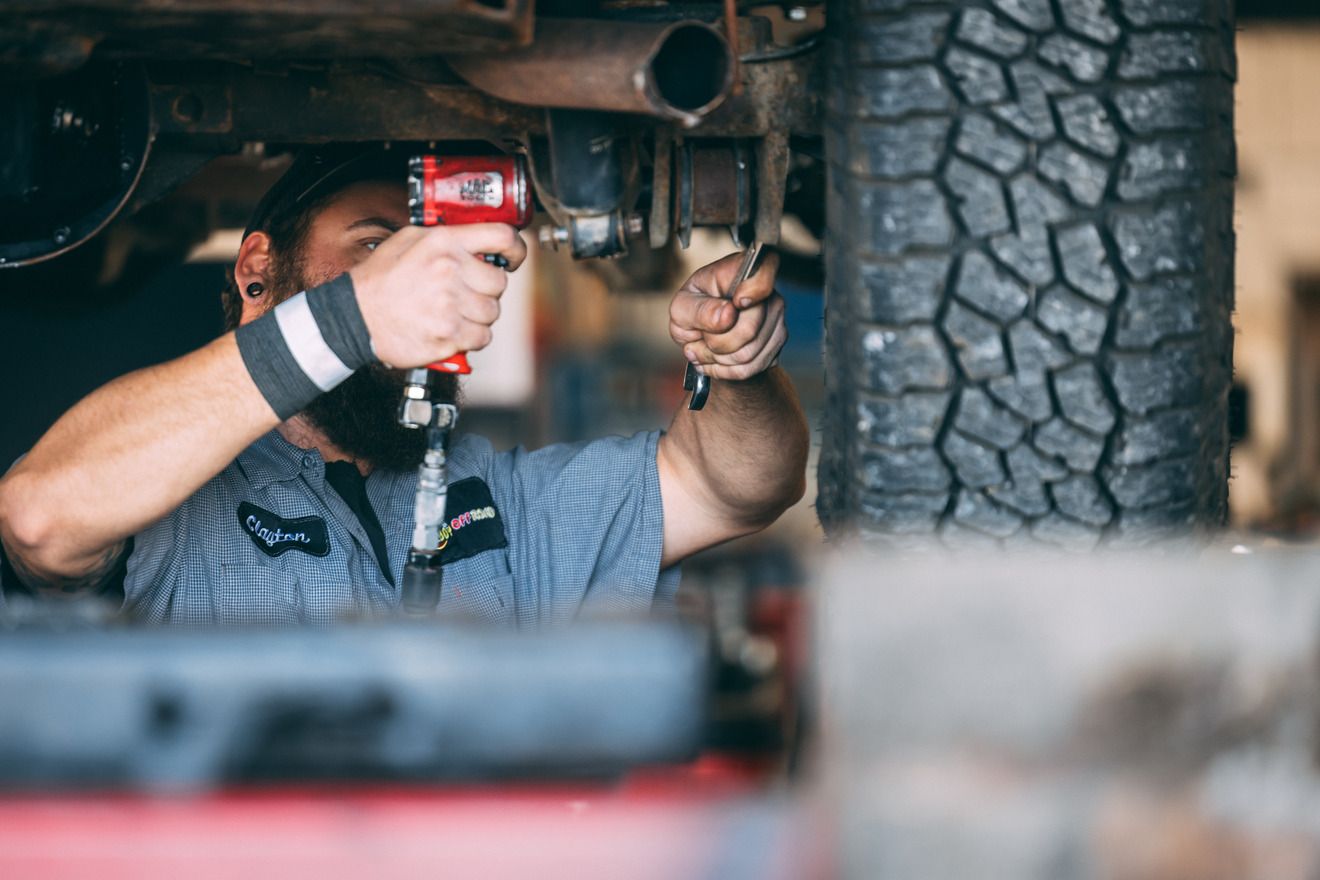 Mechanic working under a car with a power tool, in a garage.