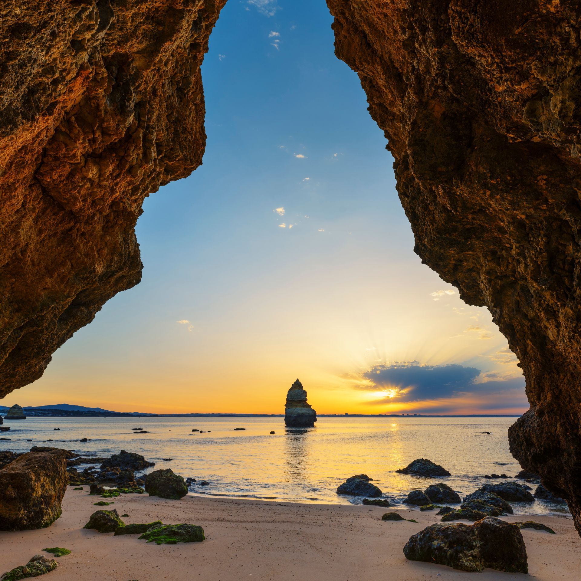 A view of a beach from a cave at sunset