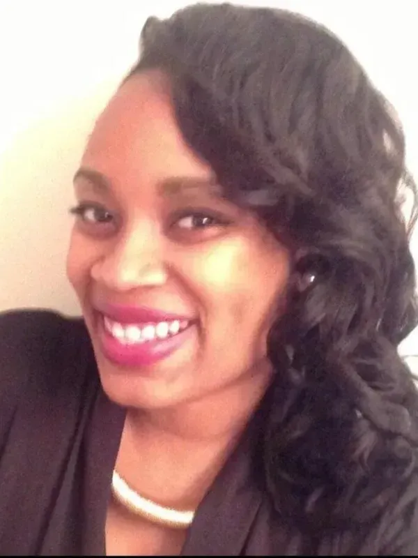 A woman wearing a black shirt and a white necklace is smiling for the camera.