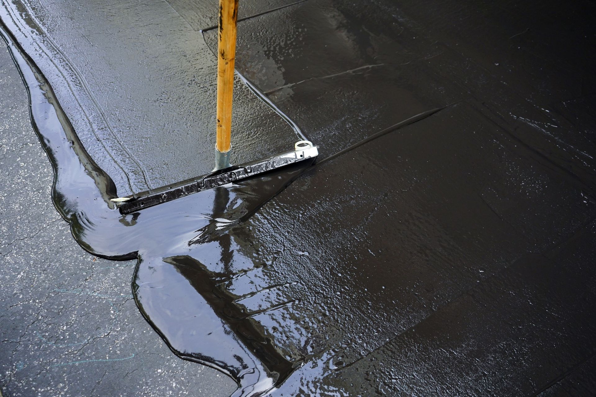 Worker spreading liquid asphalt or waterproof coating with a squeegee across pavement.