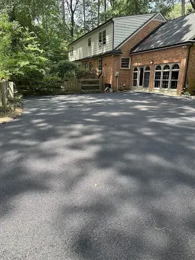 Wide driveway beside a brick-and-white house surrounded by trees and greenery