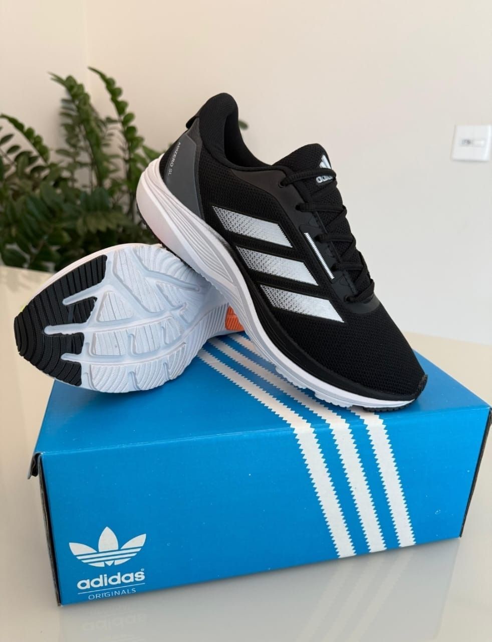 Zapatillas de running Adidas negras con rayas plateadas sobre una caja Adidas azul.