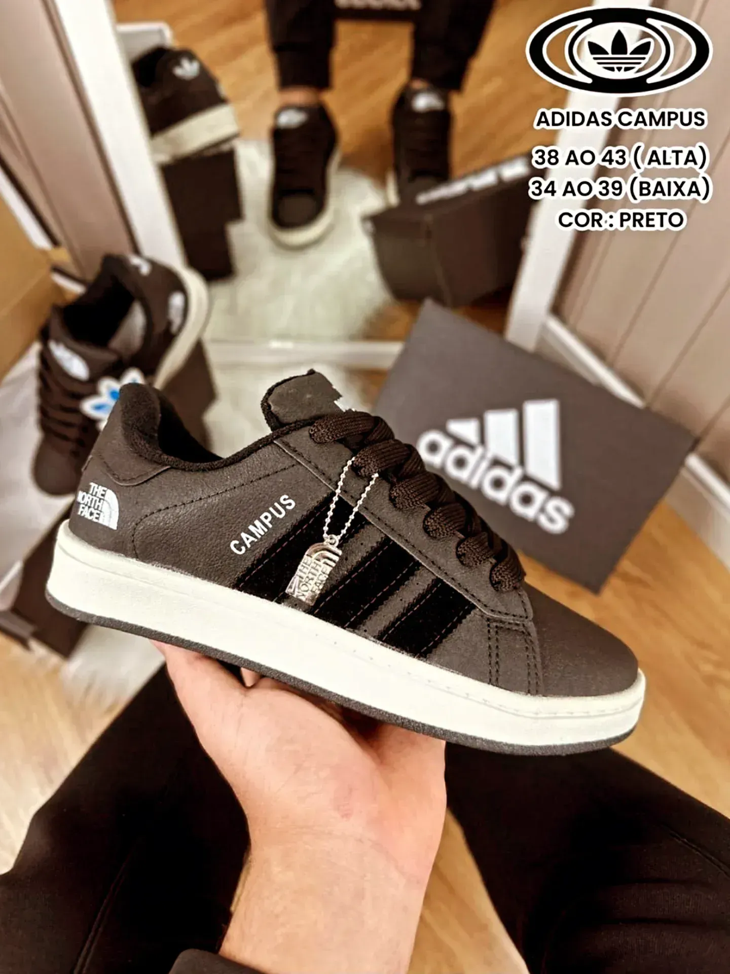 Una persona sosteniendo una zapatilla Adidas Campus negra con rayas negras, suela blanca y el texto 