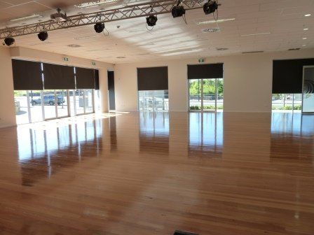 Large spacious community hall with wooden floors and glass windows allowing natural light in