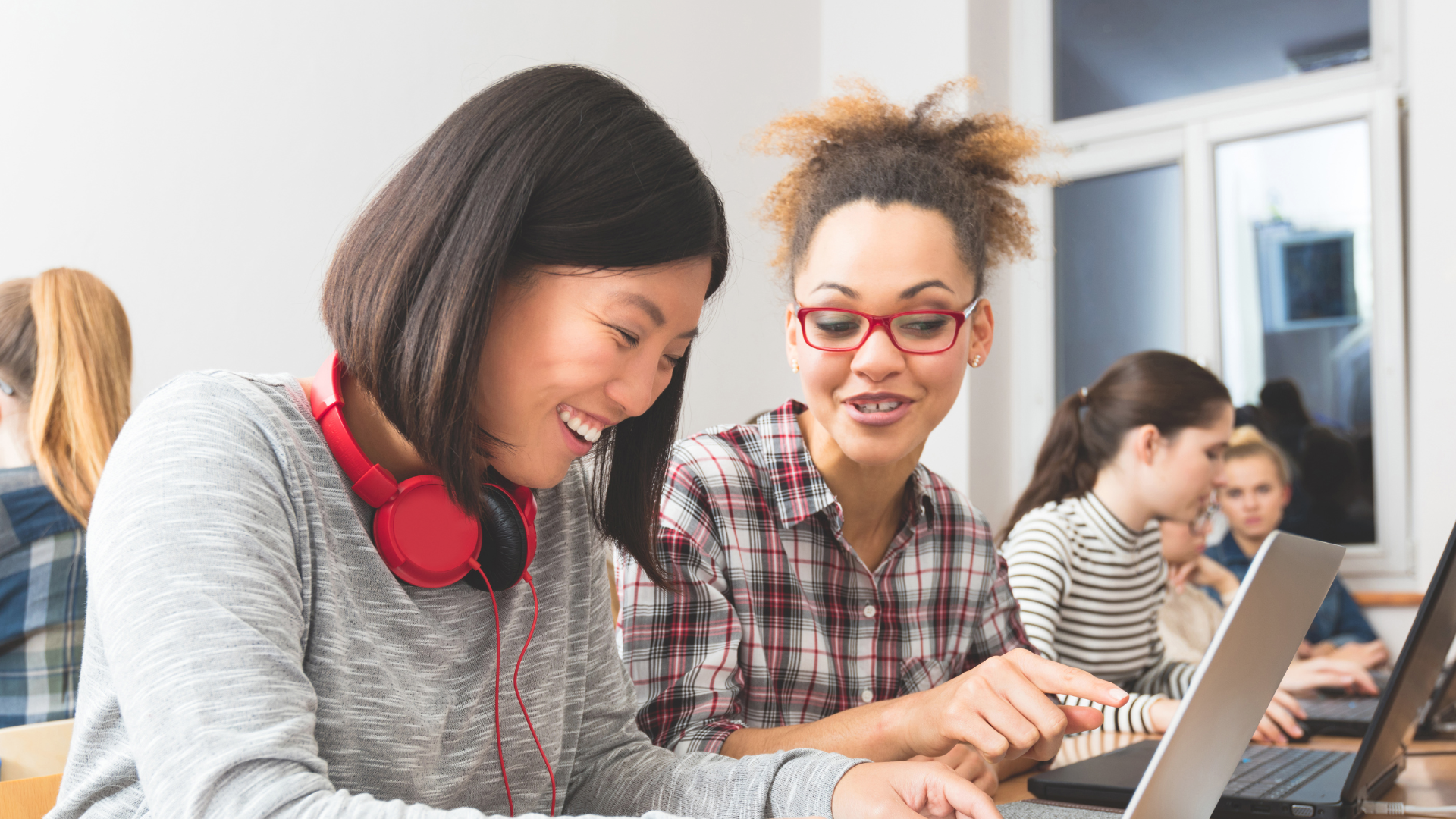 Women on laptops in a room smiling and learning together 