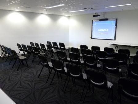 Spacious carpeted meeting room set up with rows of chairs and projector screen on showing a presentation