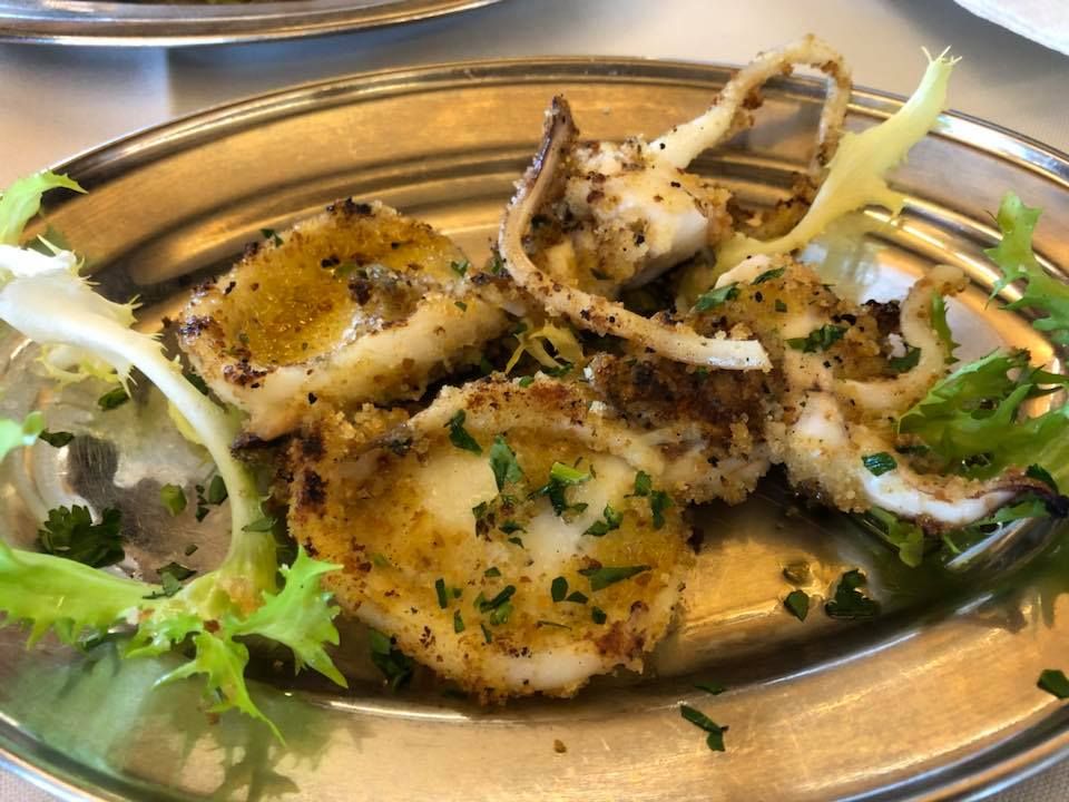 Calamari fritti su un piatto d'argento, guarniti con lattuga verde ed erbe aromatiche tritate.