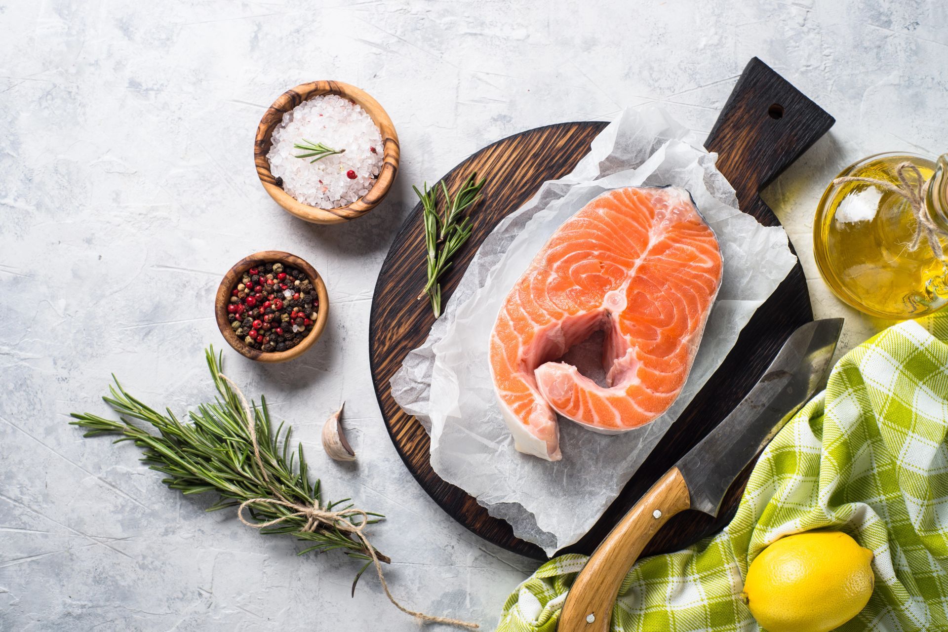 Filetto di salmone su un tagliere di legno con sale, pepe, erbe aromatiche, limone e coltello.