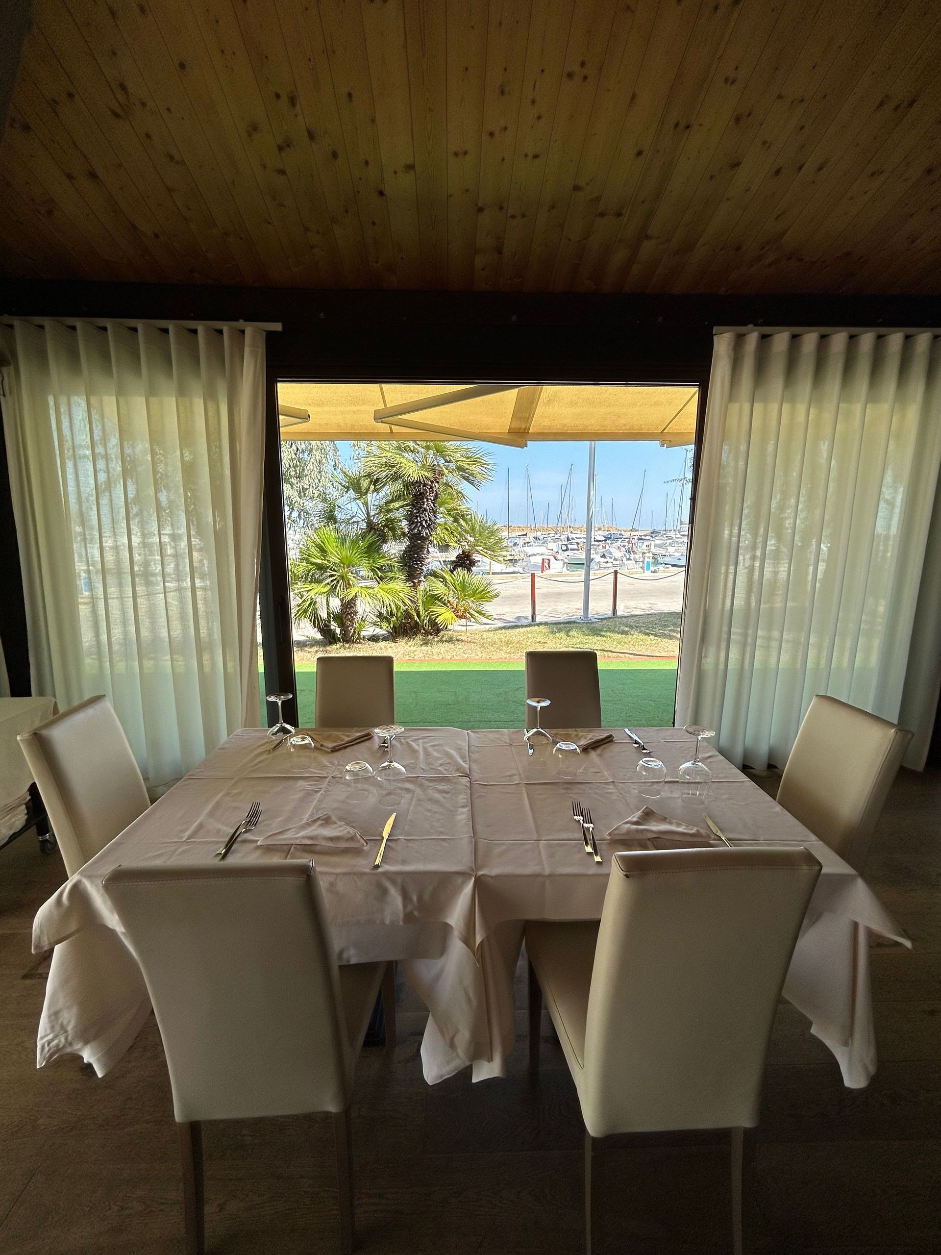 Un tavolo da pranzo apparecchiato per sei persone con vista sul prato verde, sugli alberi e sull'oceano attraverso una finestra aperta.