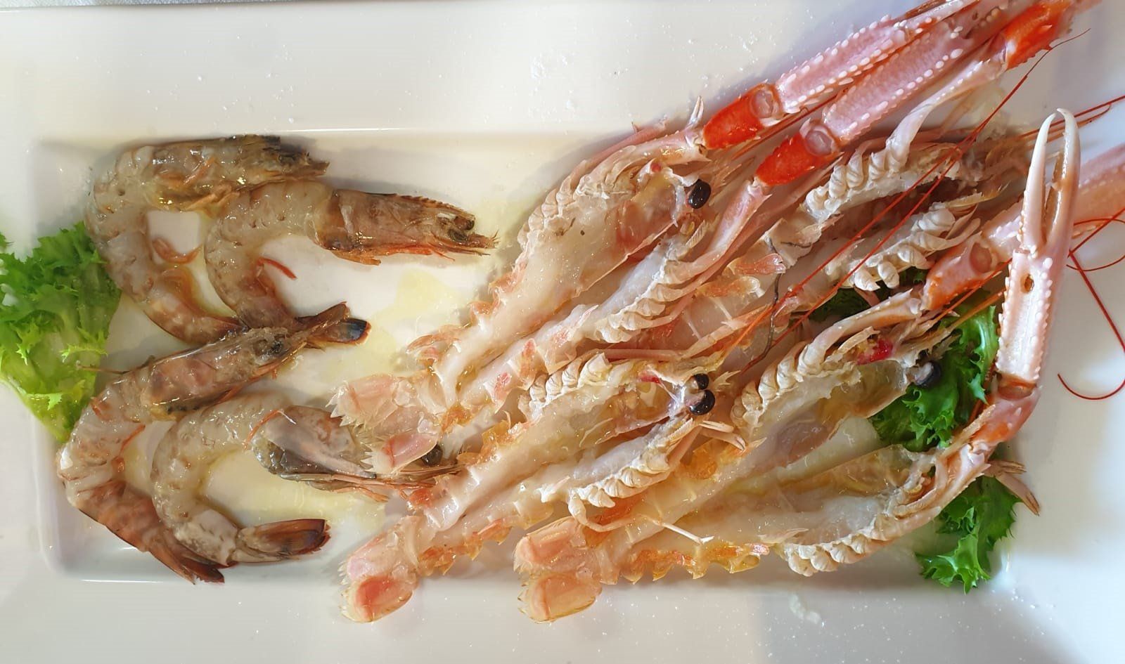 Scampi e gamberi grigliati su un piatto bianco rettangolare, guarnito con lattuga.