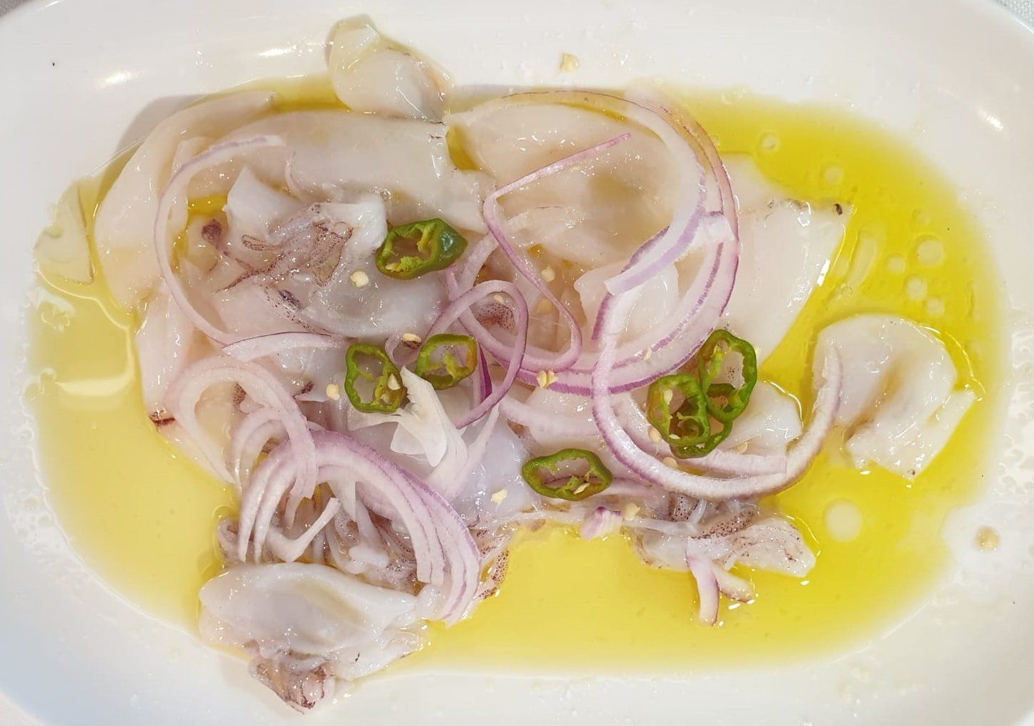 Ceviche su piatto bianco: pesce crudo con cipolla rossa, peperoni verdi e salsa gialla.