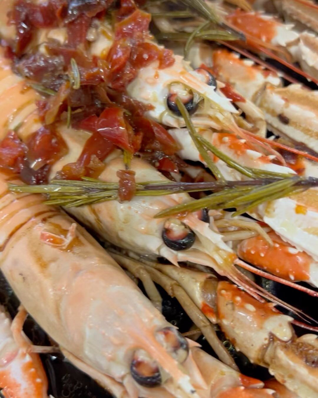 Primo piano di scampi cotti con salsa rossastra e rametti di rosmarino.