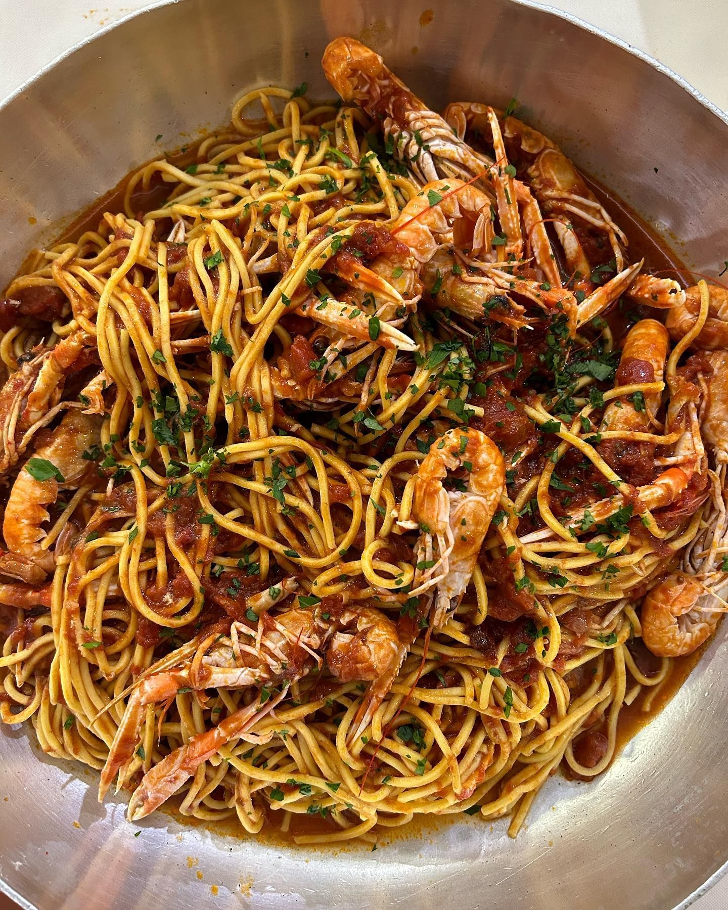 Piatto di spaghetti con gamberi in salsa di pomodoro, servito in una padella d'argento e guarnito con prezzemolo.