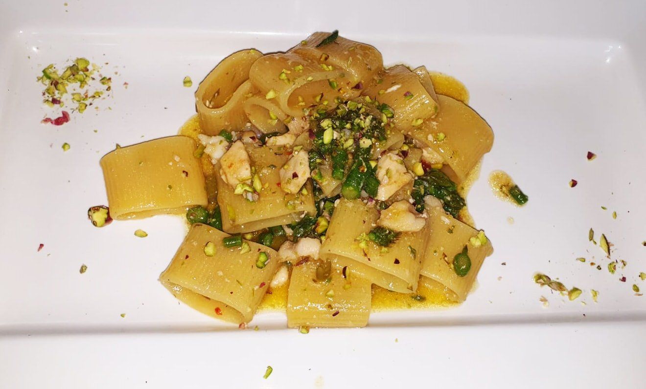 Piatto di pasta con salsa, erbe aromatiche e pistacchi su un piatto bianco rettangolare.